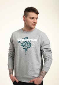 Šedá mikina vyrobená z bavlny, s grafickým potiskem s textem "WORKERWEAR" a designem v modré sprejové barvě. Dlouhé rukávy a žebrované manžety.