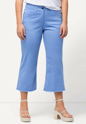 Jean cropped bleu clair avec un ourlet effiloché, poches avant et une taille ajustée, associés à des sandales à plateforme neutres avec lanières de cheville.