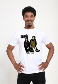 Hvid bomulds t-shirt med grafik af to siddende figurer i sort og gul, med ordet "suede" trykt med fed sort tekst.