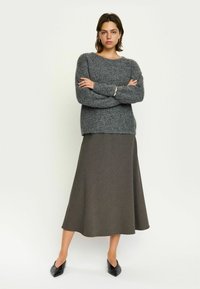 Grijze gebreide trui met een ronde hals en lange mouwen, gecombineerd met een bruine gestructureerde maxi-jurk. Zwarte schoenen met een spitse neus maken de outfit compleet.