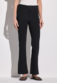Pantaloni neri a costine con vita aderente e due bottoni. Il tessuto ha una texture sottile e i pantaloni si allargano leggermente all'orlo.