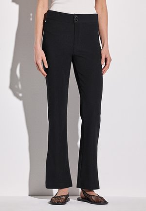 Zwarte geribbelde broeken met een aansluitende taille en twee knopen. De stof heeft een subtiele textuur en de broek heeft een lichte flare aan de zoom.