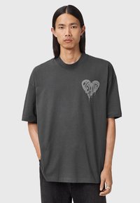 Camiseta oversized de color gris oscuro en algodón, con un gráfico de corazón goteante en gris claro en el lado izquierdo del pecho. Manga corta, cuello redondo.