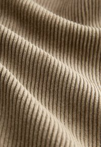 Lähedalt pildistatud beezist kangast, kus on näha pehme, ribaga tekstuur vertikaalsete soonte ja õrnade voldidega.