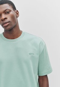 Muntgroen katoenen T-shirt met korte mouwen, voorzien van een klein, reliëf "CPH" logo op de borst en een klassieke ronde hals.