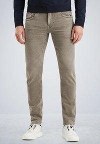 Jeans de mezclilla de corte slim en marrón claro, con cinco bolsillos y un ligero efecto desgastado, combinados con zapatillas blancas con acentos en negro y amarillo.