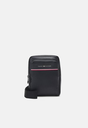 Sort rektangulær crossbody-taske med lynlåslomme foran, Tommy Hilfiger-logo og justerbar rem på hvid baggrund.