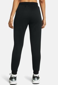 Zwarte sweatpants met een taps toelopende pasvorm, elastische tailleband en cuff aan de enkels. Ze zijn gecombineerd met sportschoenen met een grijze accent.