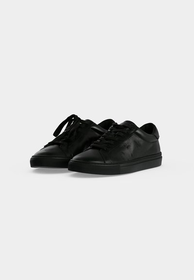 Paire de baskets basses en cuir noir avec lacets sur un fond clair uni.