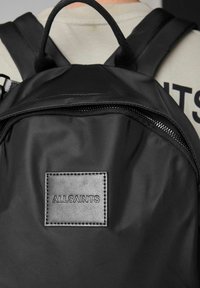 Juodas nailono kuprinės formulė su stačiakampiu odiniu pleistru, kuriame išrašytas "ALLSAINTS" logotipas, užtrauktuko uždarymu ir paminkštintais petnešomis.