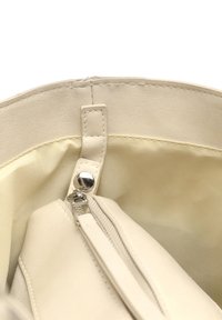 Beżowa skórzana torebka od wewnątrz o gładkiej teksturze, wyposażona w kieszeń na zamek oraz miękką podszewkę w jaśniejszym kolorze.