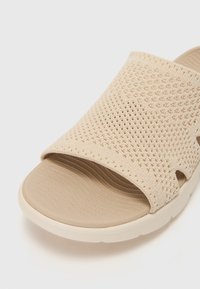 Beige sko-sandaler med et teksturert mesh-overdel, åpen design og rillede innersåler. Glatt gummisåle for komfort og fleksibilitet.