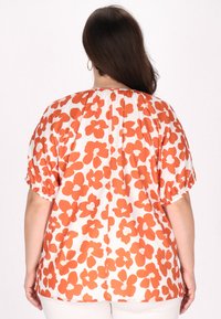 Blomstret bluse i creme med store orange blomster. Har elastiske ærmer og en samlet halsudskæring. Løst fitting design, letvægtsstof.
