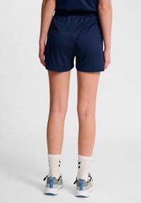 Marina atletiska shorts med elastiskt midjeband, slät textur, fållade kanter, tillsammans med grå och blå löparskor och mönstrade vita strumpor.