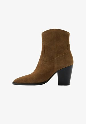 Brązowy zamszowy botek za kostkę z ostro zakończonym noskiem i grubym czarnym wysokim obcasem, z zakrzywionymi przeszyciami na cholewce.