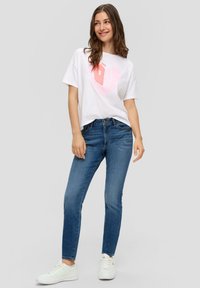 Camiseta blanca con gráfico de corazón rosa, combinada con jeans de mezclilla azul y zapatillas blancas. Conjunto casual con corte relajado y jeans de lavado medio.