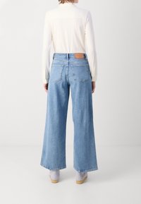 Wijd uitgevoerde blauwe denim jeans met een hoge taille, voorzien van achterzakken en een leren label bij de tailleband, gecombineerd met een witte long-sleeve shirt.