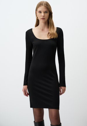 Robe noire à manches longues avec un décolleté bateau, silhouette ajustée et tissu lisse. Elle présente une longueur mi-cuisse et une texture subtile.