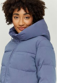 Padded jacket in soft purple with a high collar and brand logo. Features a smooth, shiny texture and visible quilted design.