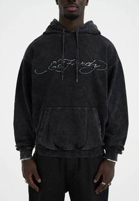 Black sweatshirt with a hood, featuring a distressed texture, front pocket, and embroidered logo. Cuffs and hem have a ribbed finish.