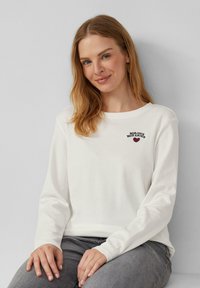 Witte lange mouwen T-shirt met geborduurde tekst "BONJOUR MON AMOUR" en een klein hartje, gecombineerd met grijze jeans; zachte katoenmateriaal.