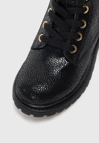 Bottines noires avec un motif de serpent texturé, œillets dorés, lacets noirs et une semelle en caoutchouc épaisse pour l'adhérence.