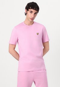 Rosa crew neck t-shirt i mjuk bomull, med en liten gul broderad fjärilslogotyp på bröstet. Korta ärmar, avslappnad passform.