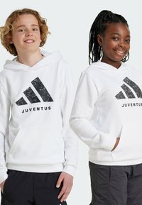 Due bambini indossano felpe bianche con il logo nero della Juventus. Le felpe hanno tasche anteriori e polsini a coste. Entrambi indossano pantaloni scuri.