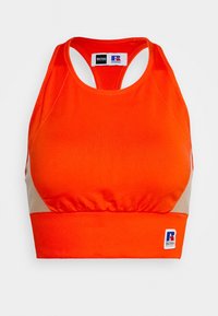 Brassière de sport en tissu orange vif avec une coupe ajustée, présentant un accent beige sur les côtés et un petit patch logo à l'ourlet.