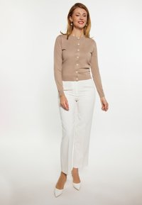 Cardigan tricotat de culoare bej deschis, cu mâneci lungi și închidere cu nasturi, asortat cu pantaloni albi cu talie înaltă, completat cu tocuri albe ascuțite.