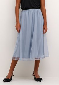 Egy világoskék, légies midi szoknya áttetsző anyagból, elasztikus derékrésszel és réteges kialakítással, fekete masnis sarkú cipővel párosítva.