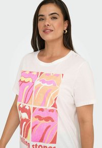 Hvid t-shirt med et farverigt grafisk print bestående af fire paneler, hver med stiliserede læber i pink og orange nuancer, med teksten "Rolling Stones."