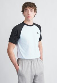 Ανδρικό T-shirt με ανοιχτό γαλάζιο σώμα και μαύρα raglan μανίκια. Περιλαμβάνει ένα μικρό μαύρο λογότυπο στο στήθος. Υλικό από απαλό βαμβάκι.