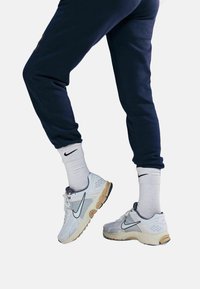 Sneakers Nike w białej siateczce z szarymi akcentami, z grubą beżową podeszwą, w połączeniu z białymi skarpetkami w prążki i granatowymi dresami.