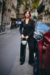 Noor naine mustas ülikonnas, kes hoiab hõbedast südamekujulist rahakotti, seisab linnatänaval parkivate autode ja taustal oleva kohviku vahel.