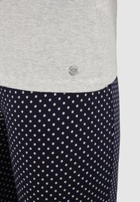 Hellgraues Oberteil mit Rundhalsausschnitt, kombiniert mit marineblauen Hosen, die weiße Punkte aufweisen und ein kleines metallisches Logo nahe der Taille tragen.