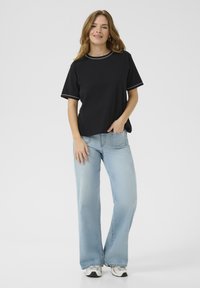 Sort kortærmet t-shirt med hvid kant, parret med lyseblå brede jeans, der viser en afslappet pasform og en uformel stil.
