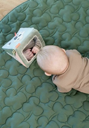 Hladký zelený prešívaný hrací koberec s vyvýšenými vzorami oblakov. Neďaleko leží plyšový domček s zrkadlom a farebnými akcentmi, ktorý odráža detské ruky.