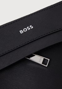 Czarna torebka z teksturowanej skóry z metalowym zapięciem i logo "BOSS". Charakteryzuje się prostymi liniami i minimalistycznym designem. Wykonana z trwałego materiału z wyrafinowanymi detalami.