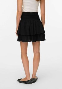 Svart lagdelt skjørt med smocket midje, laget av lett stoff. Utslått design med en avslappet passform som når til midt på låret.