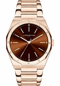 Montre octogonale en or rose avec un cadran marron et des index en argent. Dotée d'un bracelet en maillons métalliques et d'un design minimaliste.