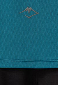 Maglia sportiva color teal con tessuto testurizzato, orlo arrotondato e un sottile logo grigio posizionato vicino al collo.