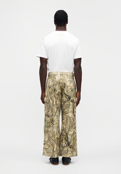 Παντελόνια cargo με καμουφλάζ σε αποχρώσεις καφέ και πράσινου. Χαλαρή εφαρμογή, με πλαϊνές τσέπες και ψηλή μέση. Λευκό μπλουζάκι.