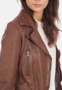 Brun läderbikerjacka med en dragkedjeficka, snapskrage och strukturerad yta. Utrustad med silverfärgad hårdvara och sidodragkedjestängning.