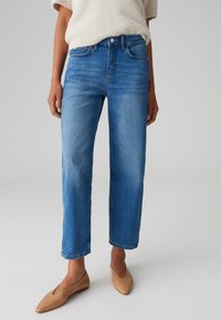 Jeans in denim blu con taglio dritto, lavaggio chiaro, leggere sfumature, e un classico design a cinque tasche, abbinati a ballerine beige.