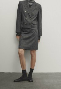 Grå ullblandad dubbelknäppt blazer med guldknappar, kombinerad med en figurnära grå kjol. Svarta strumpor och ballerinas fulländar outfiten.