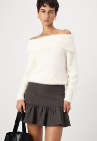 Pulover z dolgimi rokavi v beli barvi, ki se nosi čez ramena in je puhast, v kombinaciji z oprijetim mini krilom v rjavih pinstripes, ki ima nabran rob. Črna torba v roki.