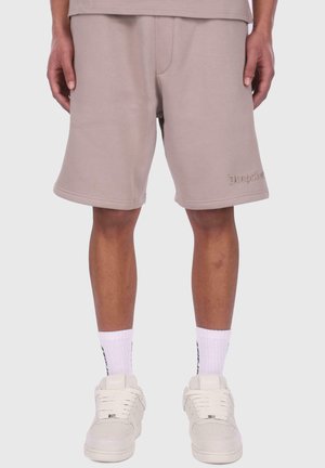 Beige katoenen shorts in een relaxte pasvorm, met een klein logo-detail aan de zoom, gecombineerd met witte sportsokken en sneakers.