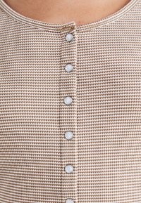 Gros plan sur une chemise tricotée beige et blanche texturée avec six boutons blancs sur le devant et un col arrondi.