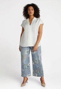 Blusa bianca a maniche corte con colletto. Abbinata a jeans ampi a fiori blu chiaro e scarpe con tacco beige.